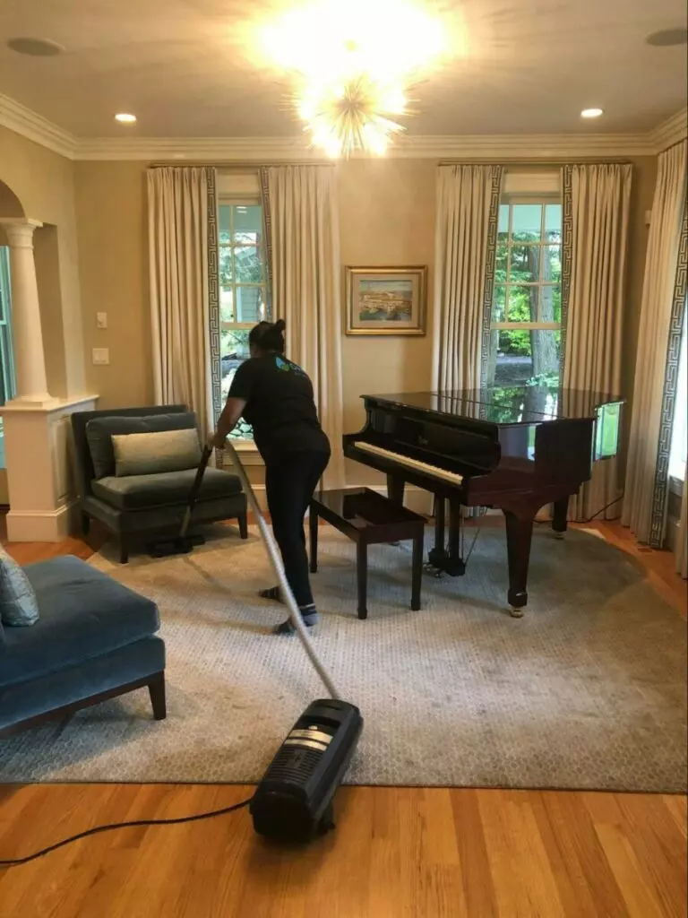 A woman from a cleaning company in Boston meticulously cleans a living room with a vacuum.