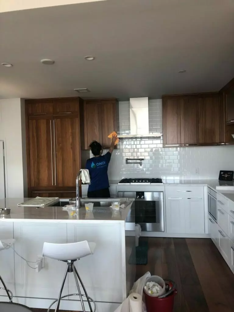 A man is working in a kitchen with white cabinets for a cleaning company in Boston.