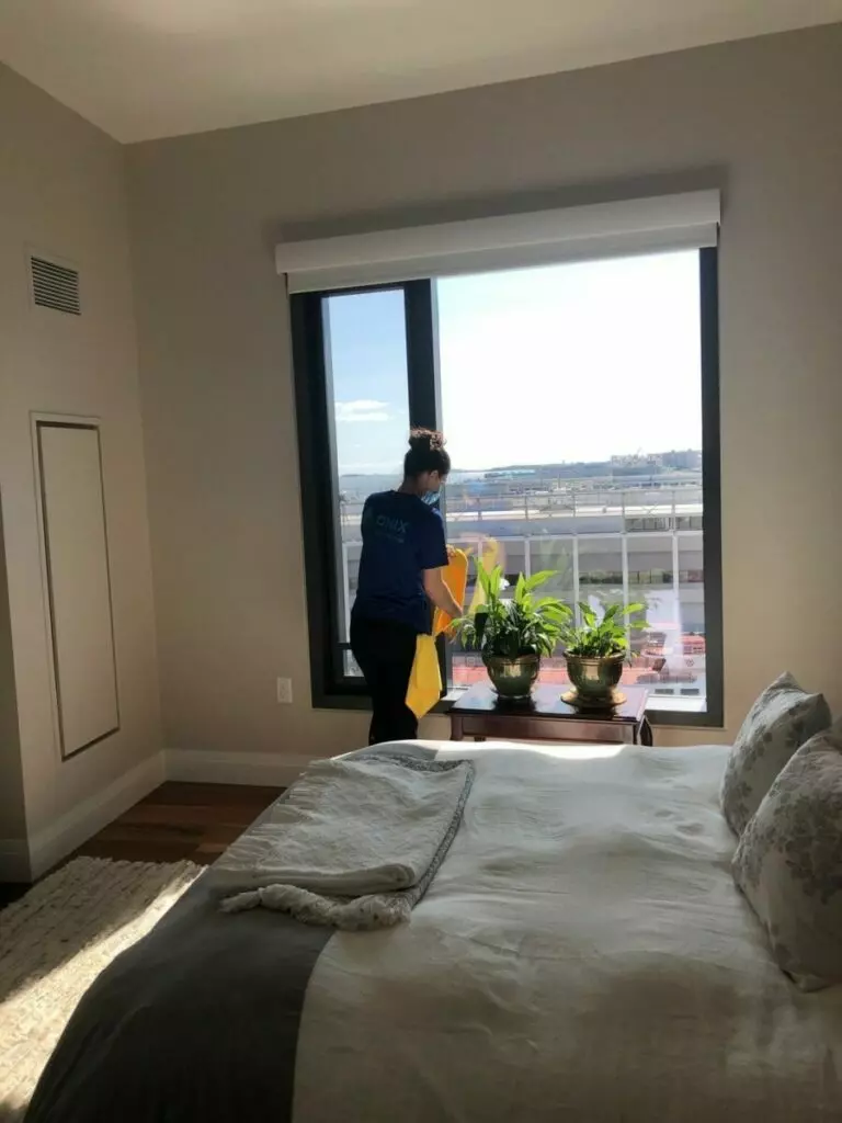 A woman providing maid service in a bedroom with a window view.