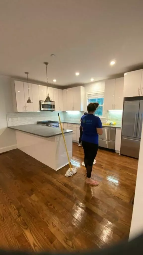 A woman diligently cleaning a kitchen floor with a mop, providing her expert Cleaning Services Boston.