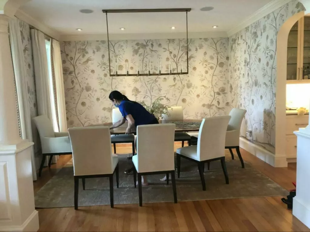 A woman from Boston cleaning a dining room with wallpaper.