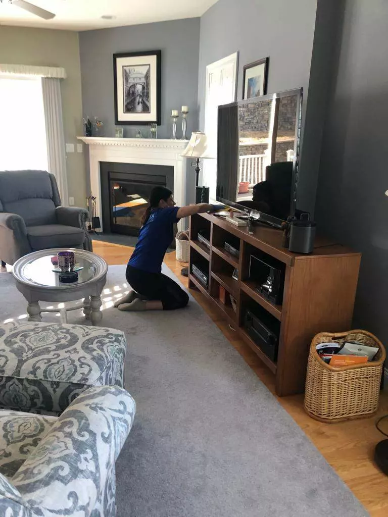 A man providing Cleaning Services in Boston, tidying up a living room with a TV.