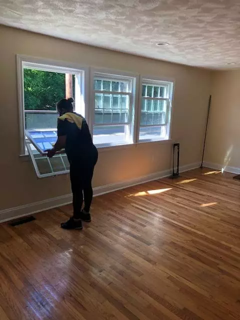 A woman cleaning a window in a room with hardwood floors in Boston.