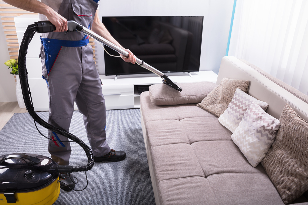 a man cleaning the sofa using a vaccum cleaner