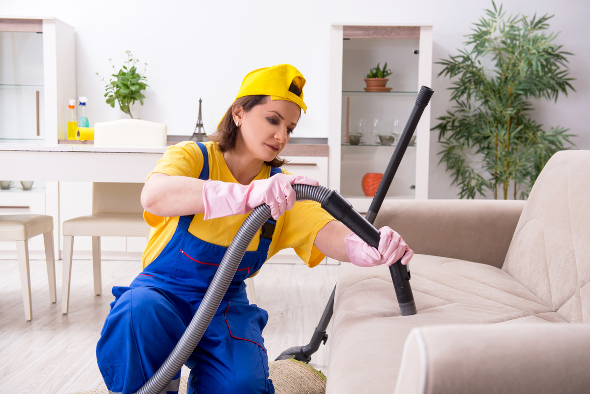 a female contractor cleaning the couch using a vacuum