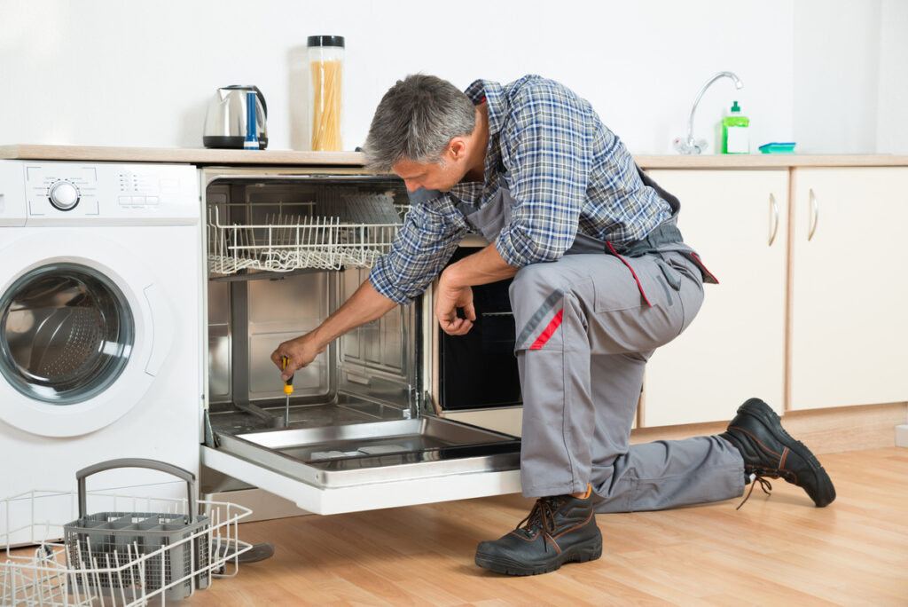 a man repairing a damaged dishwasher cabinet