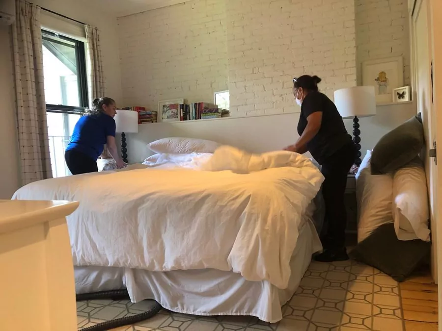 two female cleaners assisting each other in neatly arranging a blanket in a bedroom