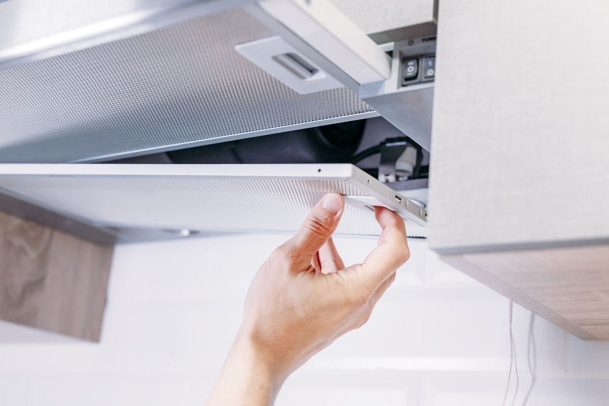 an image showing a person's hands delicately taking off the kitchen exhaust fan cover