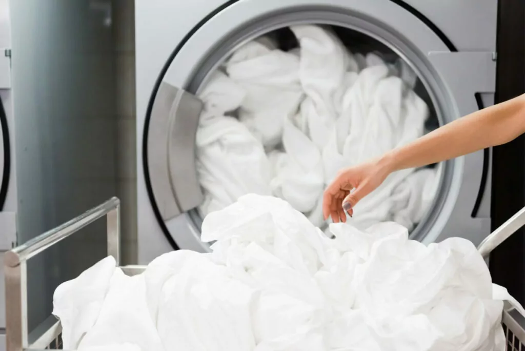 an image of a hand carefully removing freshly washed bed sheets from a washing machine
