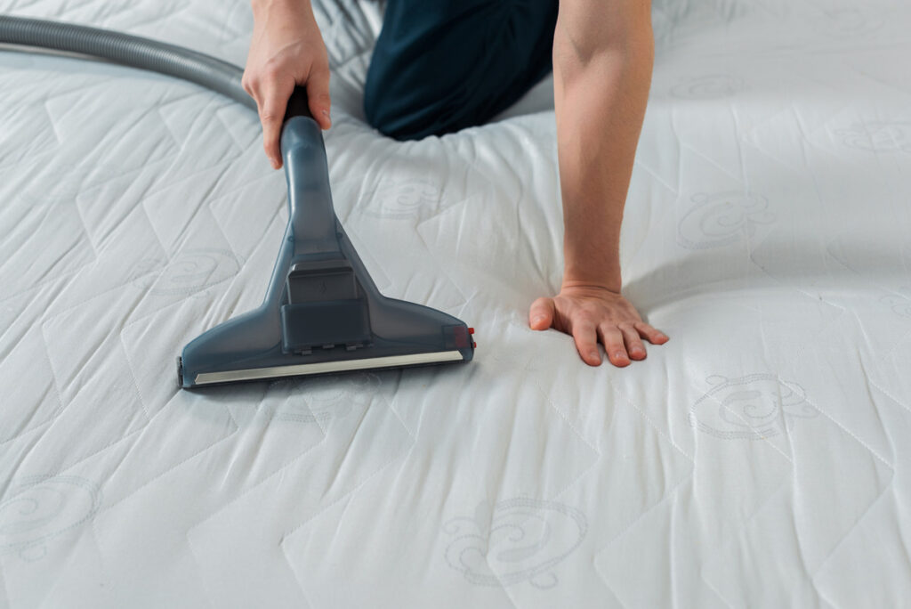 a picture of a male cleaner vacuuming a mattress