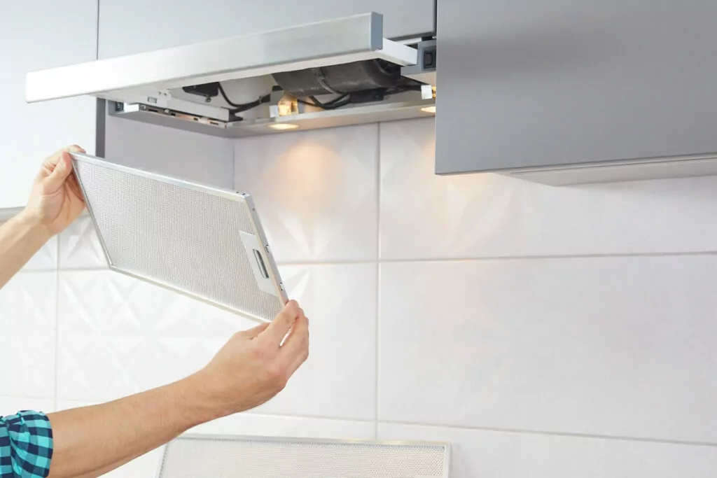 photograph showing a pair of hands grasping the kitchen exhaust fan cover as it is being removed