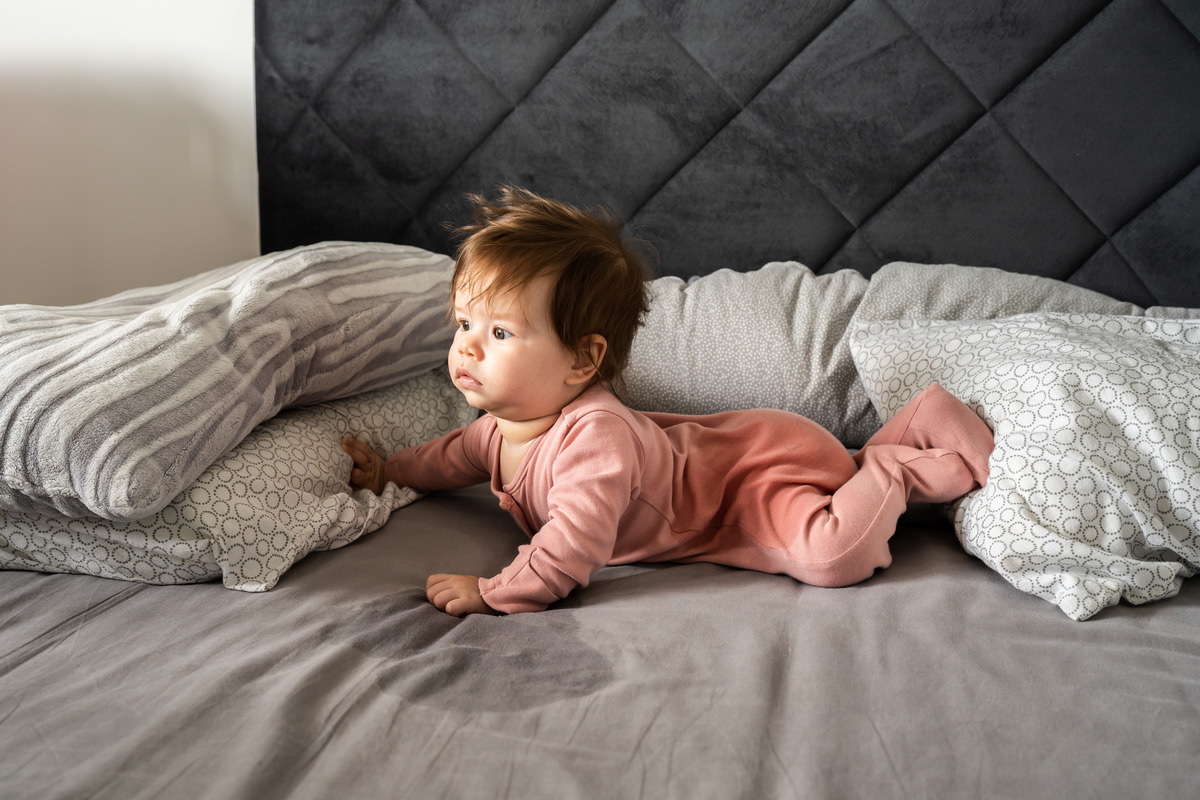 an image of a baby lying on their stomach on a mattress with a wet spot