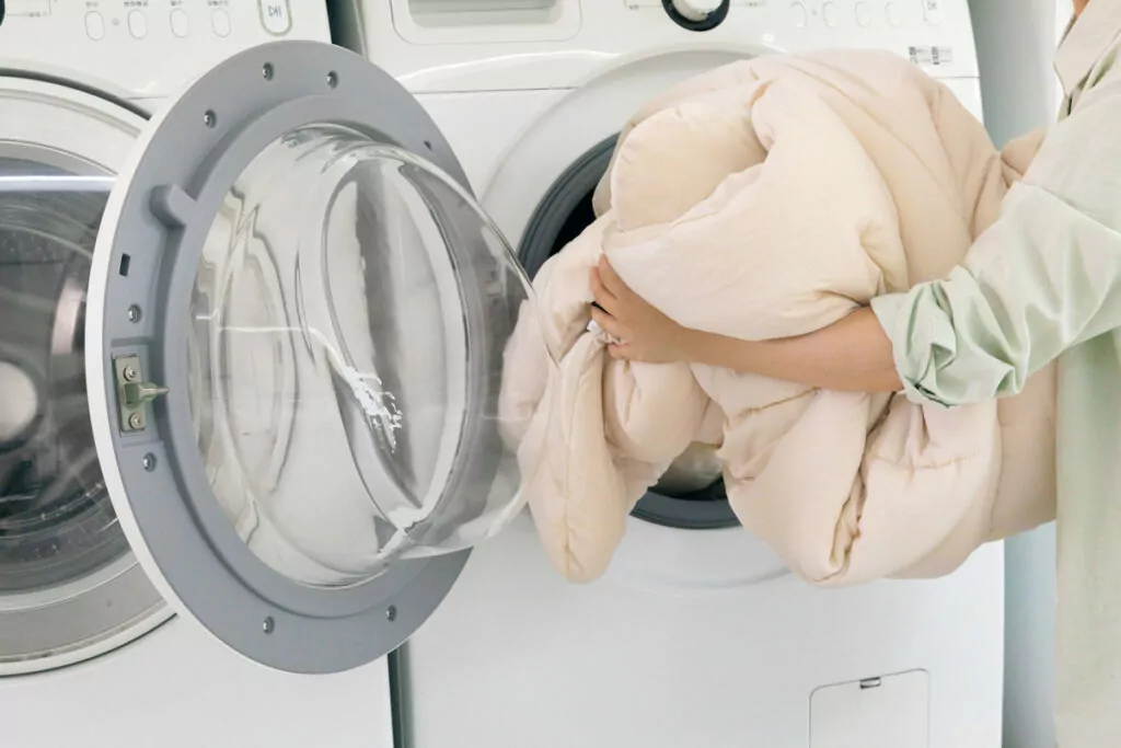 an image of a hand carefully placing a blanket into the front loading compartment of a washing machine