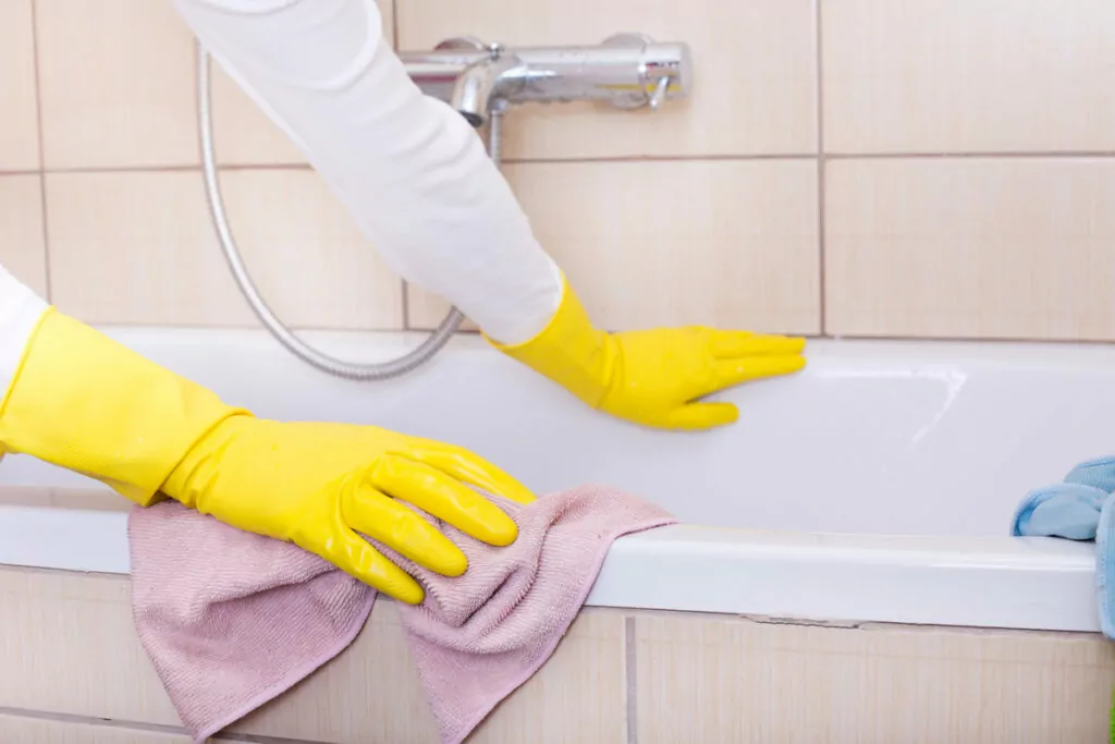 a pair of gloved hands belonging to a woman, diligently wiping down the surface of a bathtub