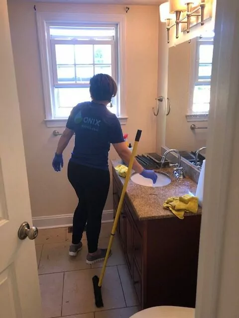 female Onix cleaner with gloved hands getting ready to clean a bathroom with a mop and a piece of cloth