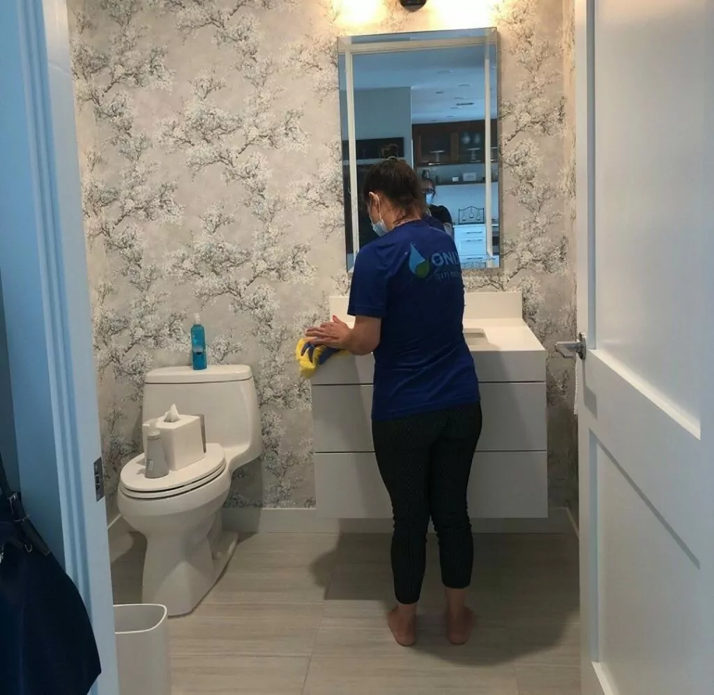 an image of a female Onix cleaner, cleaning the bathroom sink next to the toilet bowl