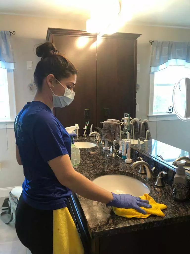 an image of a woman onix cleaner wearing a cleaning glove as she wipes the bathroom countertop next to the sink