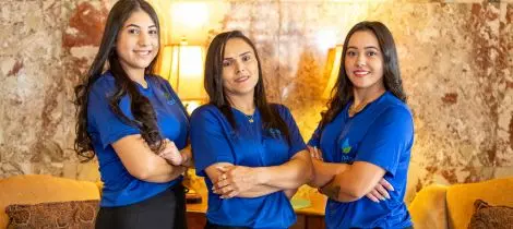 Three women in blue shirts standing in front of a couch.