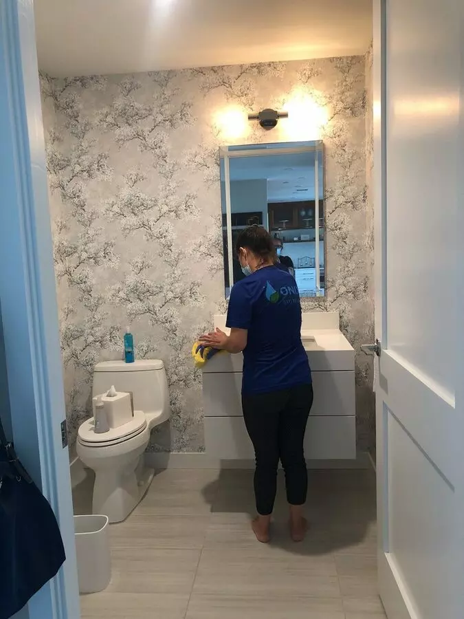 A woman in a blue shirt meticulously cleaning a bathroom.Keywords: bathroom cleaning