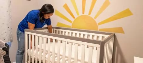 A woman setting up a crib in a room with a sun painted on the wall.