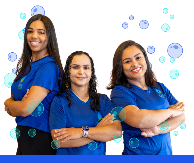 Three women in blue shirts standing in front of a blue background, providing cleaning services for Airbnb properties.