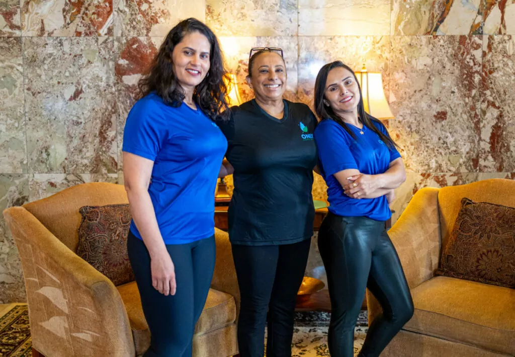 Three women in blue shirts posing in front of a couch.