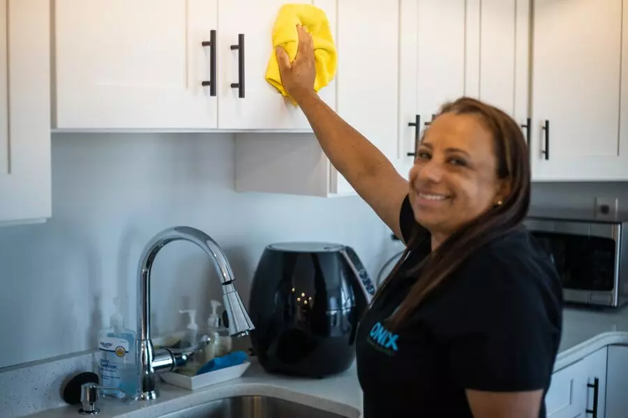 An apartment cleaning template being used by a woman to clean a kitchen.