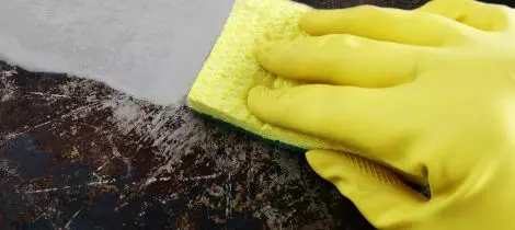 A person wearing a yellow rubber glove deep cleaning a granite countertop.