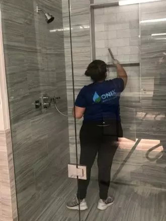 A woman cleaning a glass shower door before a move out.
