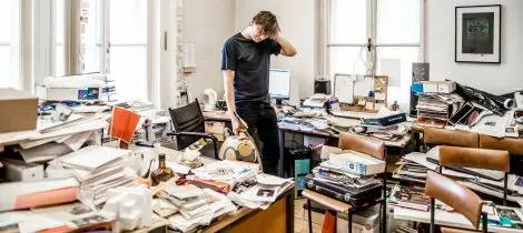 A man standing in front of a disorganized office, contemplating the need for office cleaning.