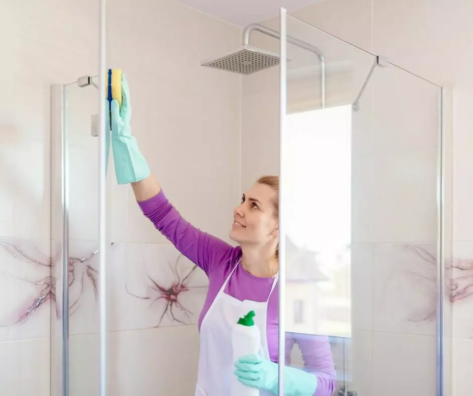 A woman cleaning a shower with a sponge using the Onix Cleaning service.