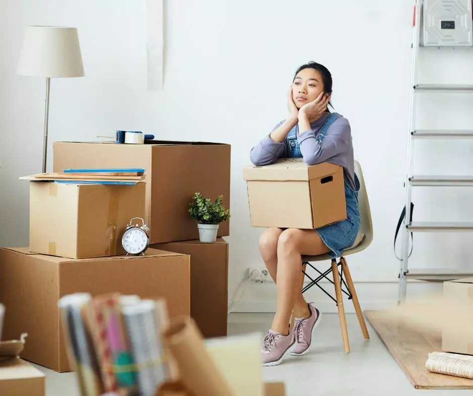 A woman sits on a chair in a room with boxes, possibly ready to move out or move in.
