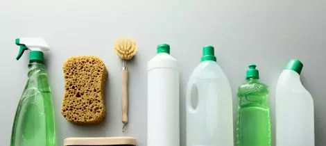 Various green cleaning supplies and a sponge arranged in a line against a neutral background.