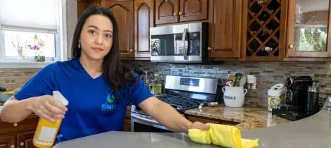 A person wiping a kitchen countertop with house cleaning spray and cloth.