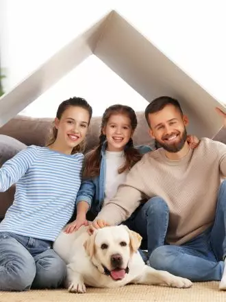 A smiling family with a child and a labrador retriever sitting under a symbolic house cleaning templates paper roof.
