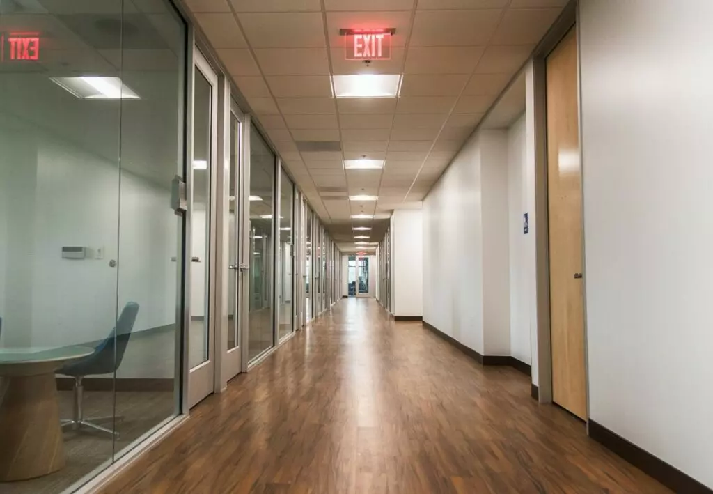 A hallway in an office with glass walls and wooden floors, maintained by commercial cleaning services.