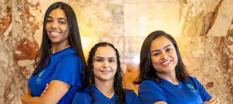 Three smiling women in blue shirts, representing house cleaning templates, standing in a row against a marble background.