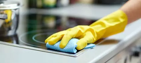 A woman in yellow gloves following standard cleaning templates to clean a stovetop.
