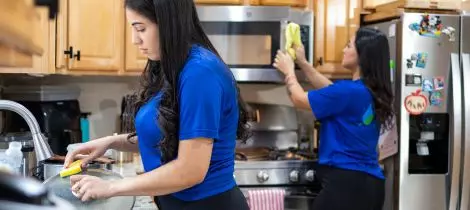 Two women cleaning a kitchen in blue shirts according to their recurring cleaning templates.