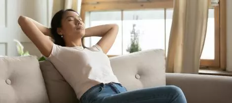 A woman is relaxing on a couch at home after finishing her standard cleaning.