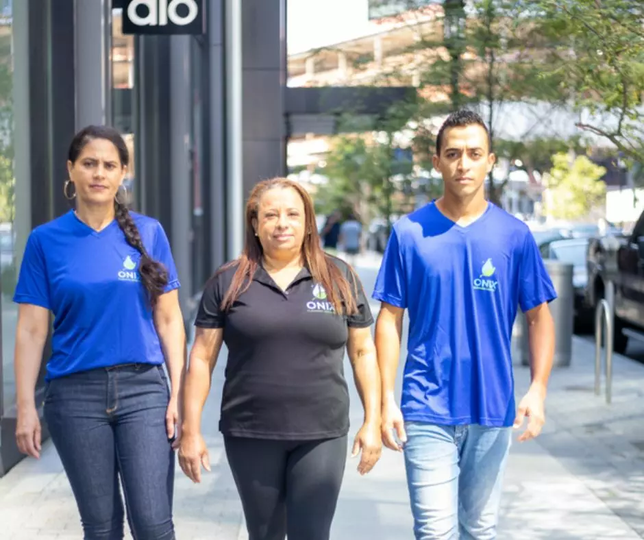 Three individuals wearing green cleaning company shirts walking on a city sidewalk.