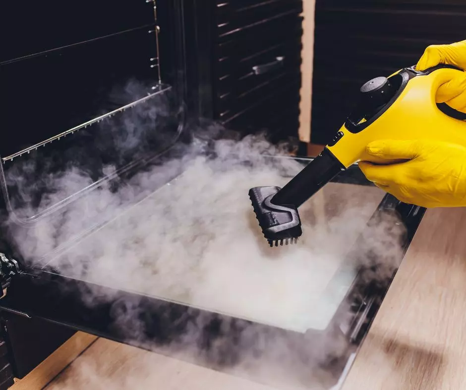 A person sanitizing an oven with a steam cleaner.