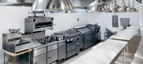 A professional stainless steel kitchen with industrial stoves, hoods, and countertops, meticulously clean and organized according to a strict cleaning schedule.