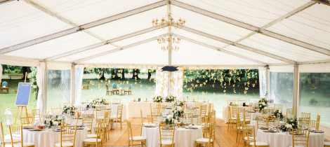 Elegant outdoor event setup under a white marquee with chandeliers, floral centerpieces, and round dining tables, complete with special event cleaning templates for impeccable maintenance.
