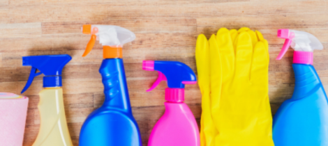 Assorted cleaning supplies, including spray bottles and rubber gloves, arranged on a wooden surface for special event cleaning.